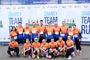 Group photo of the running team in orange and blue running shirts in front of the official HafenCityRun 2025 banner.